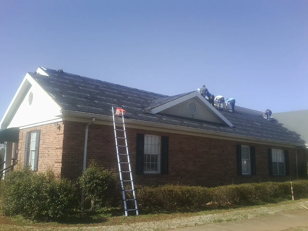 Crew tearing shingles off a brick ranch roof with a ladder set — Emergency Roof Repair work by our crew in Rolling Meadows