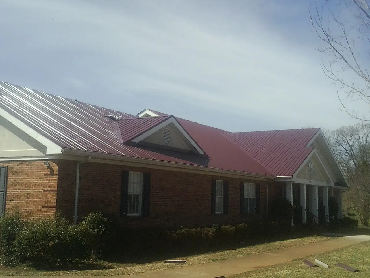 Red metal roof with gabled entries on a long brick building, from a Hail Damage Roof Repair job in Rolling Meadows
