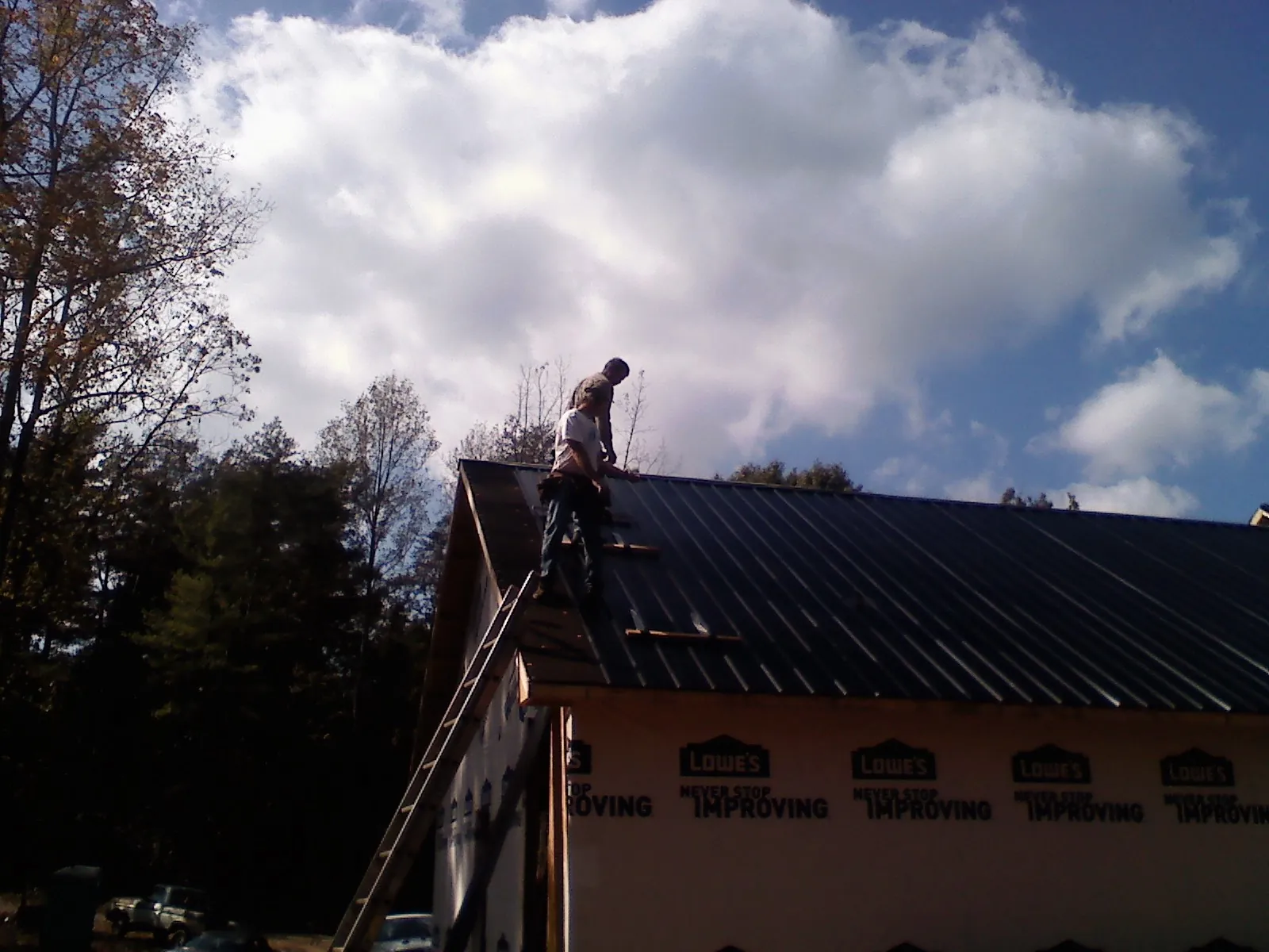 Roofer fastening dark metal panels high against a cloudy sky, from a Roof Inspection job in Rolling Meadows